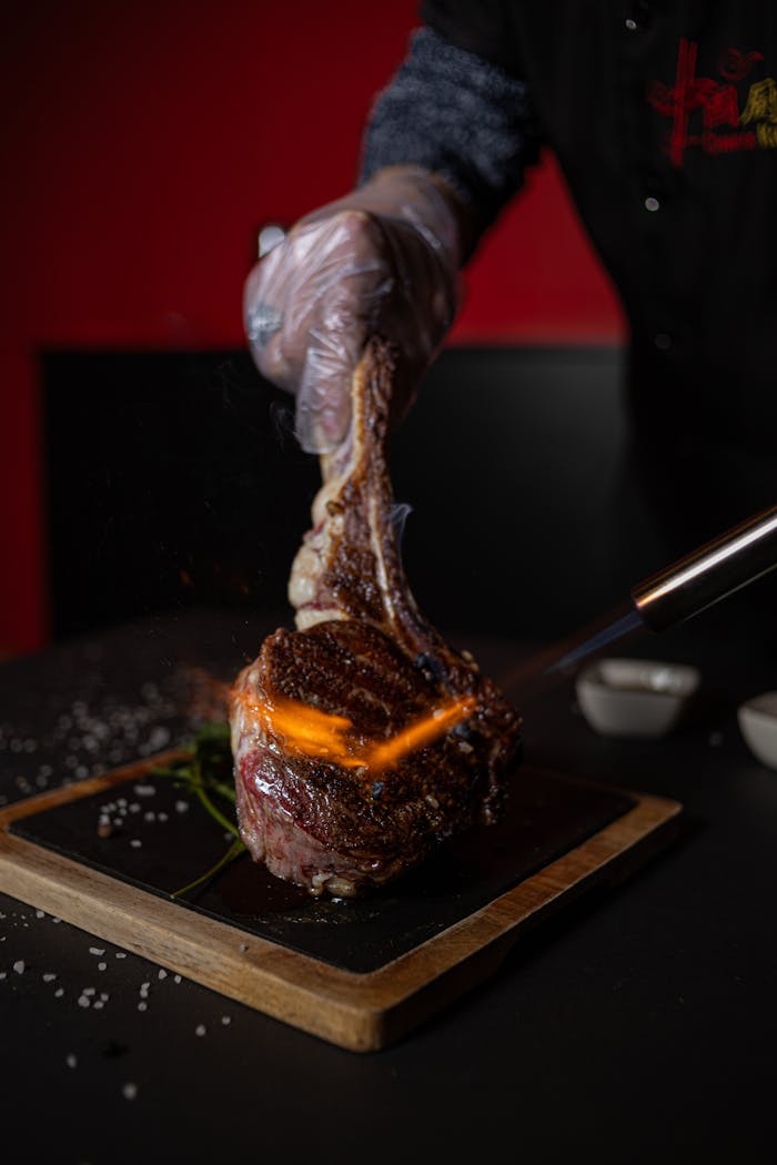 who-we-are-03 A chef expertly sears a Tomahawk steak with a torch, creating a delicious caramelized crust.